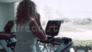 老年妇女在健身房的跑步机上订婚。 女人在电话里说话做跑步机